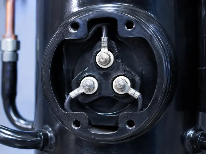 Close-up of a compressor's three small fusite terminals, the highest-current electrical connection point in an air conditioning unit.