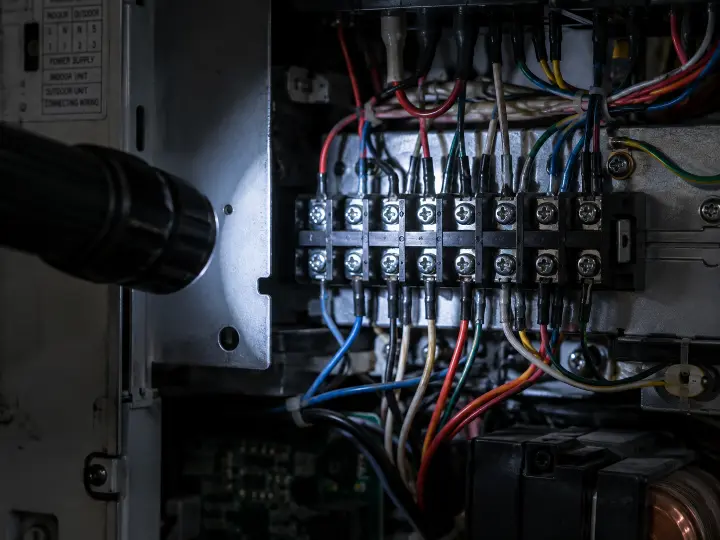Electrical terminal and connection point inside an open air conditioning service panel, illuminated during a routine inspection.