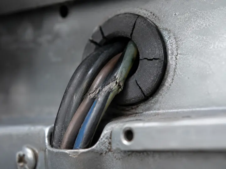 Wire bundle passing through a panel penetration with a cracked rubber grommet, insulation worn thin from years of vibration against the metal edge.